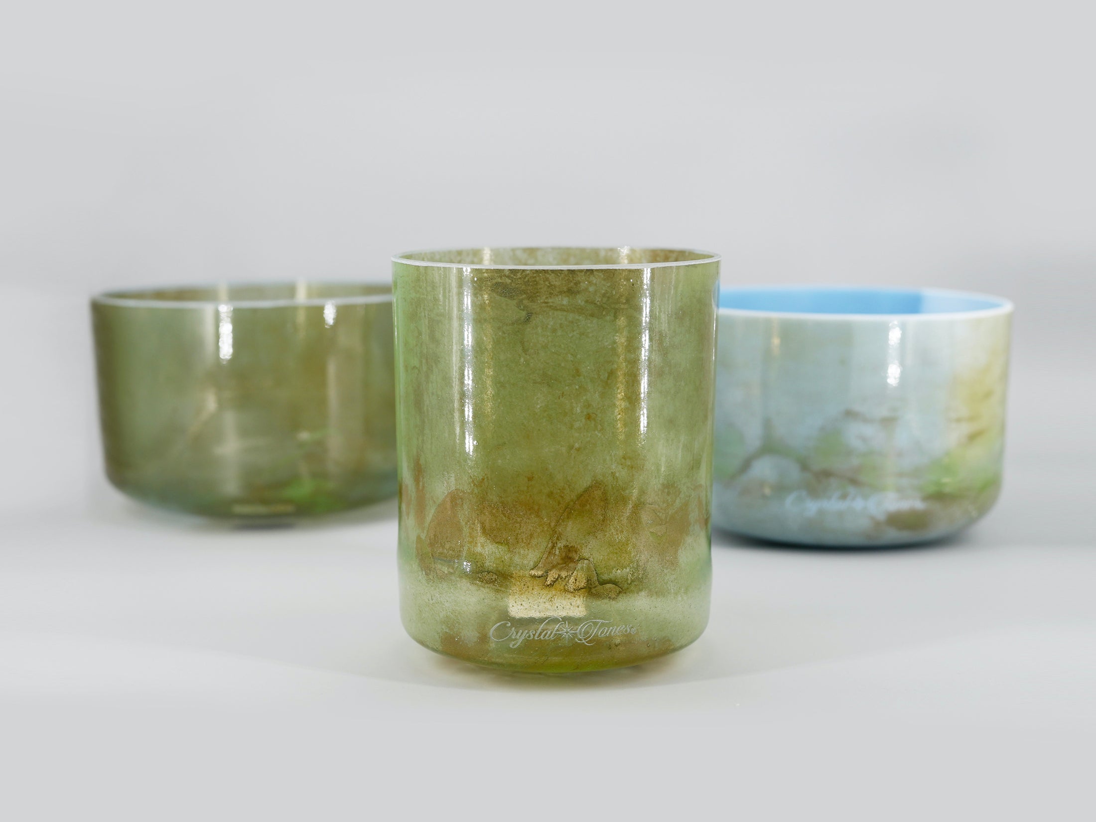 Enchanted Forest 3 bowl harmonised set of Alchemy Crystal Tones Quartz Singing Bowls. Three bowls with green and blue hues on a light grey background.