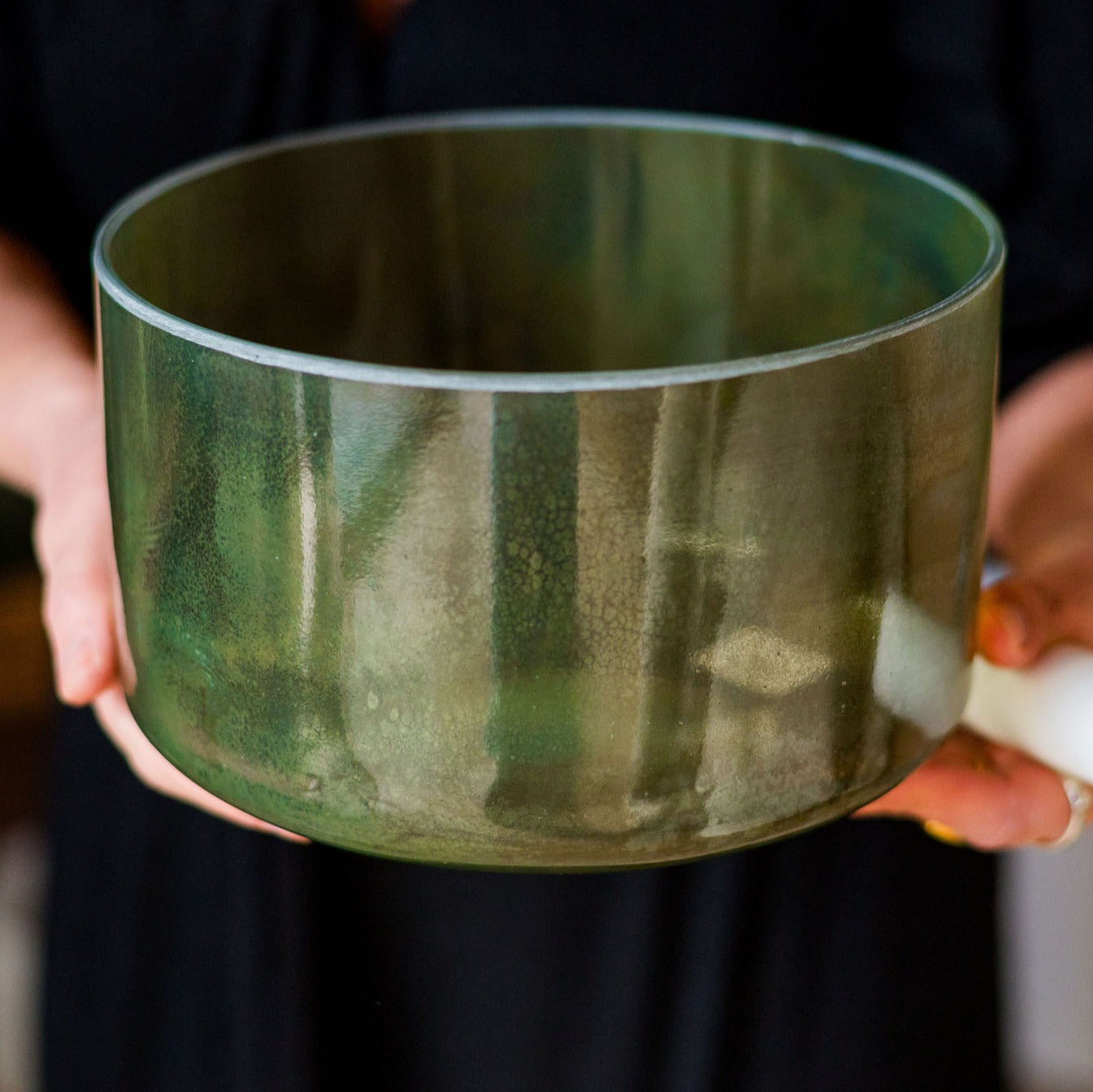 Person holding a green crystal sound bowl with a blurred background