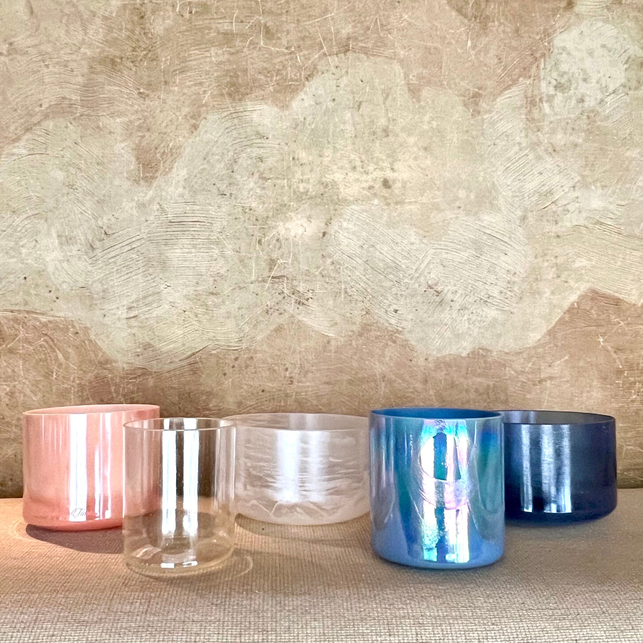 Four Crystal Sound Bowls on a textured surface with a textured wall background