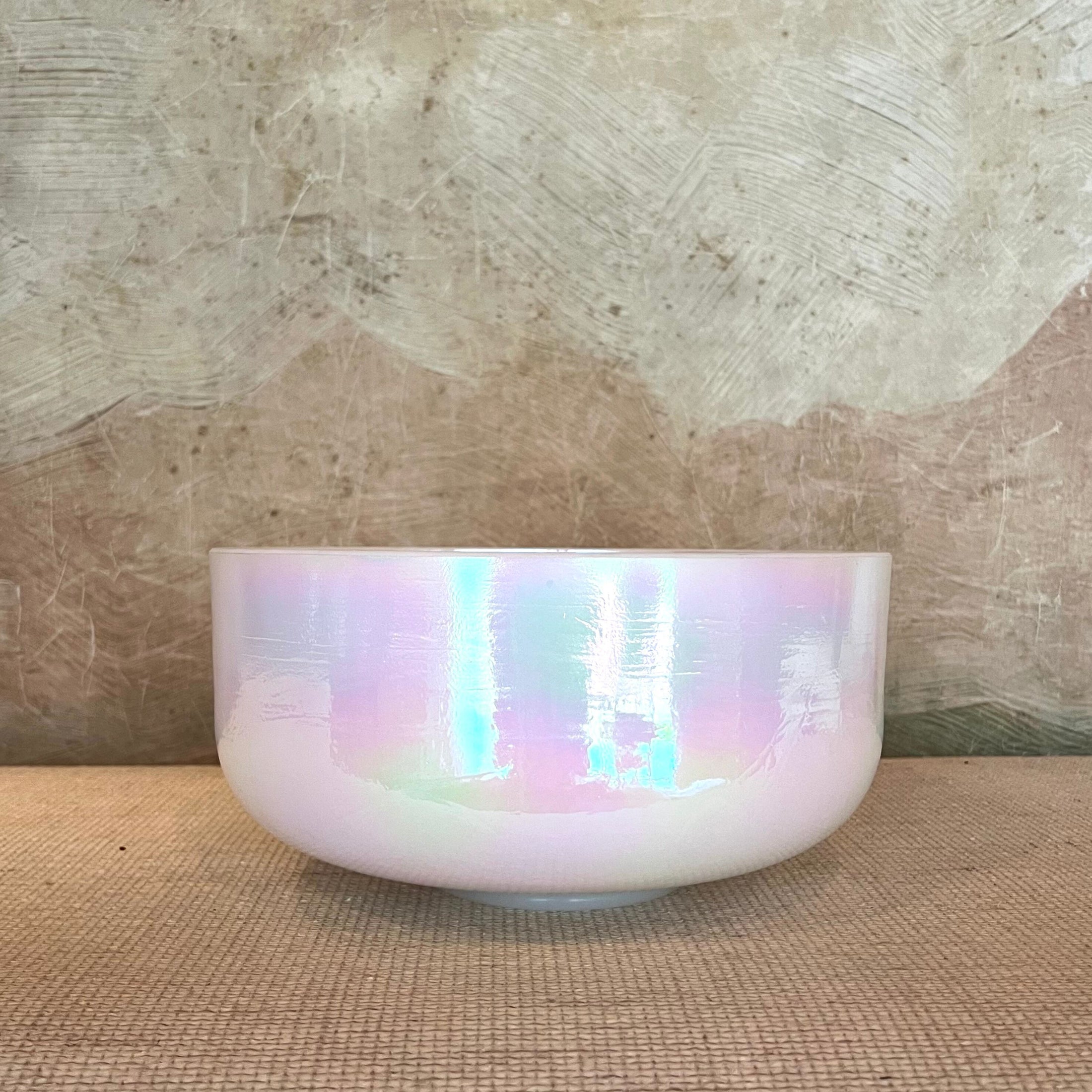 Iridescent crystal sound bowl on a textured surface with a neutral background