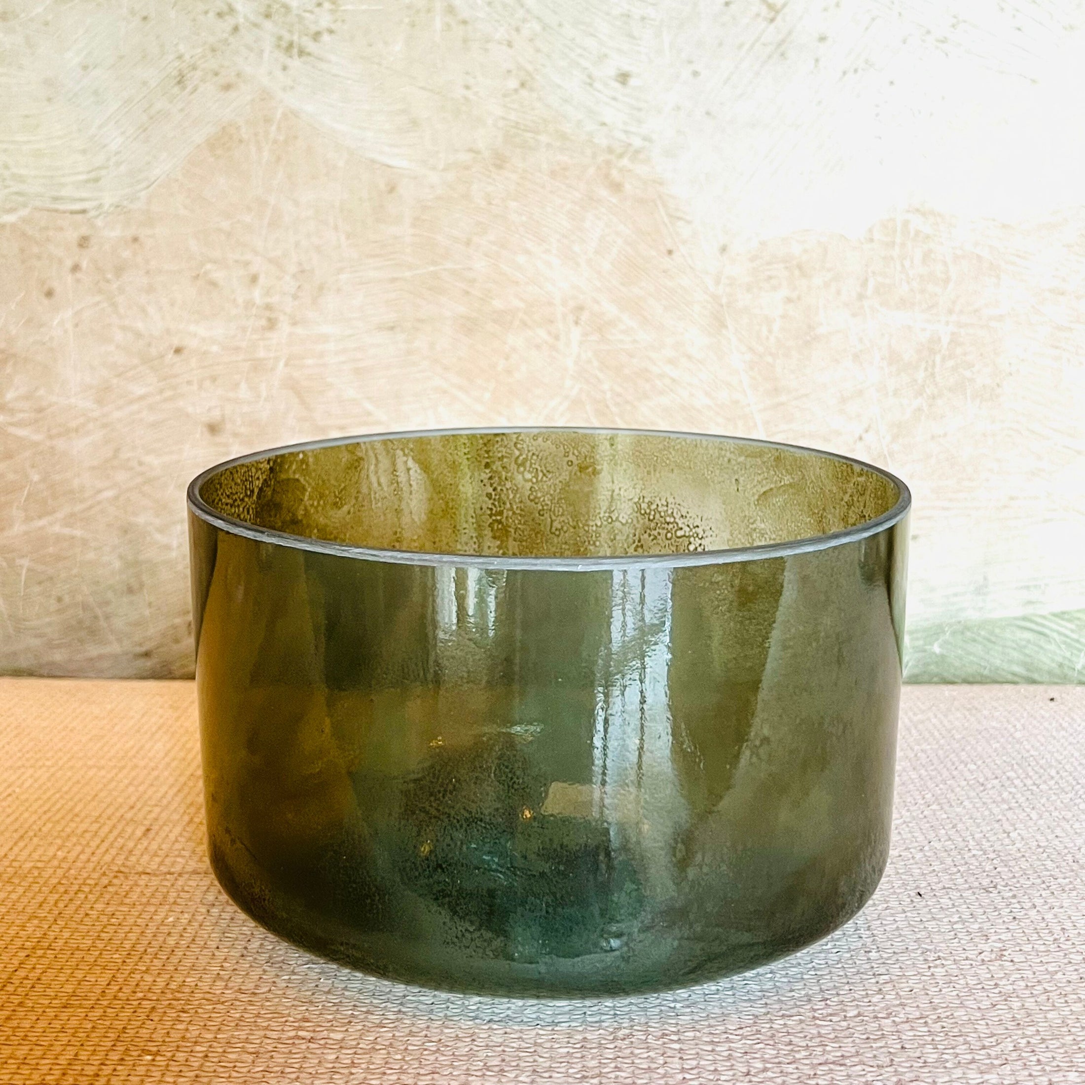 Green crystal sound bowl on a textured surface with a neutral background