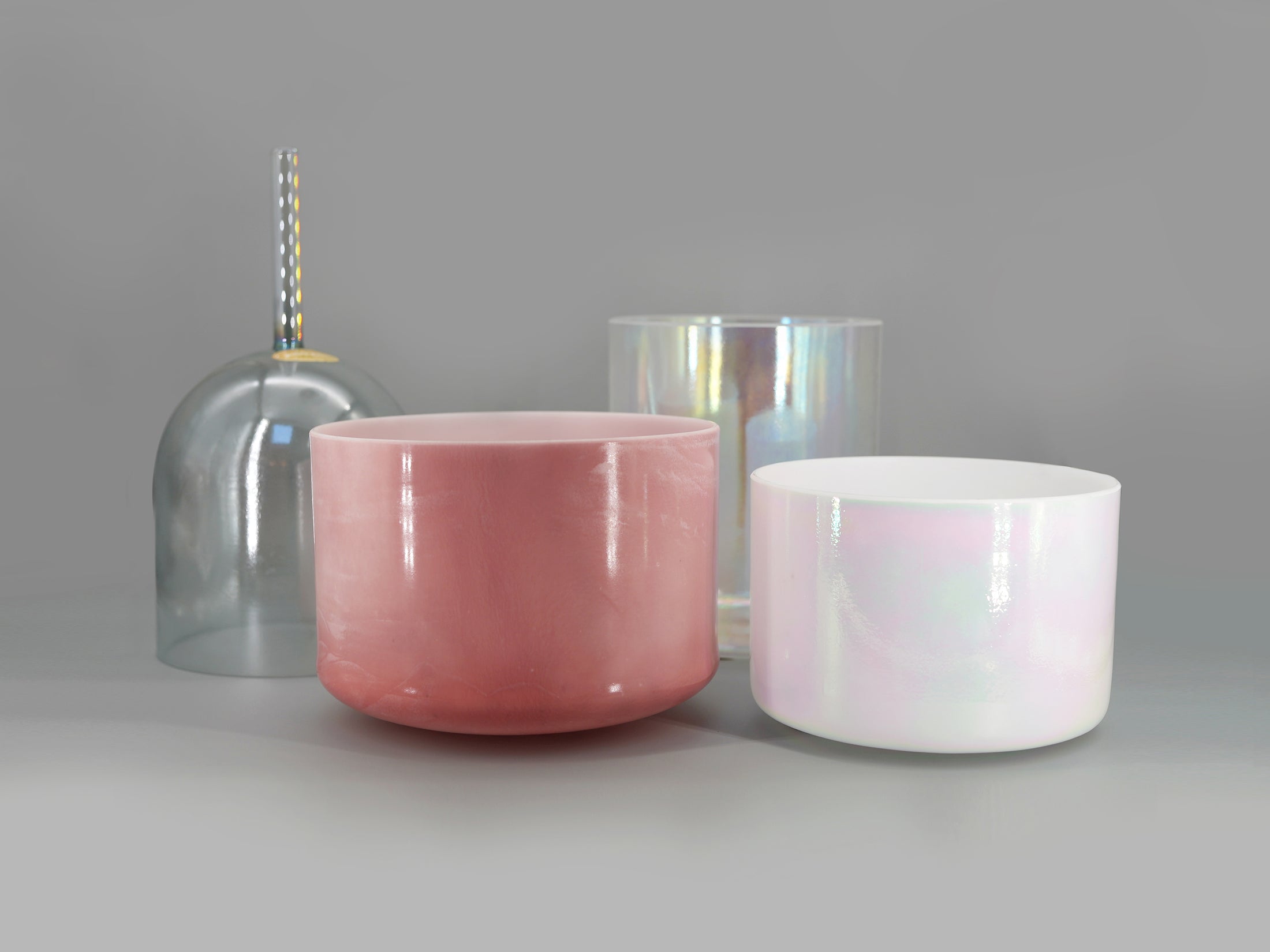 Four crystal sound bowl in pink, white, and clear glass on a gray background