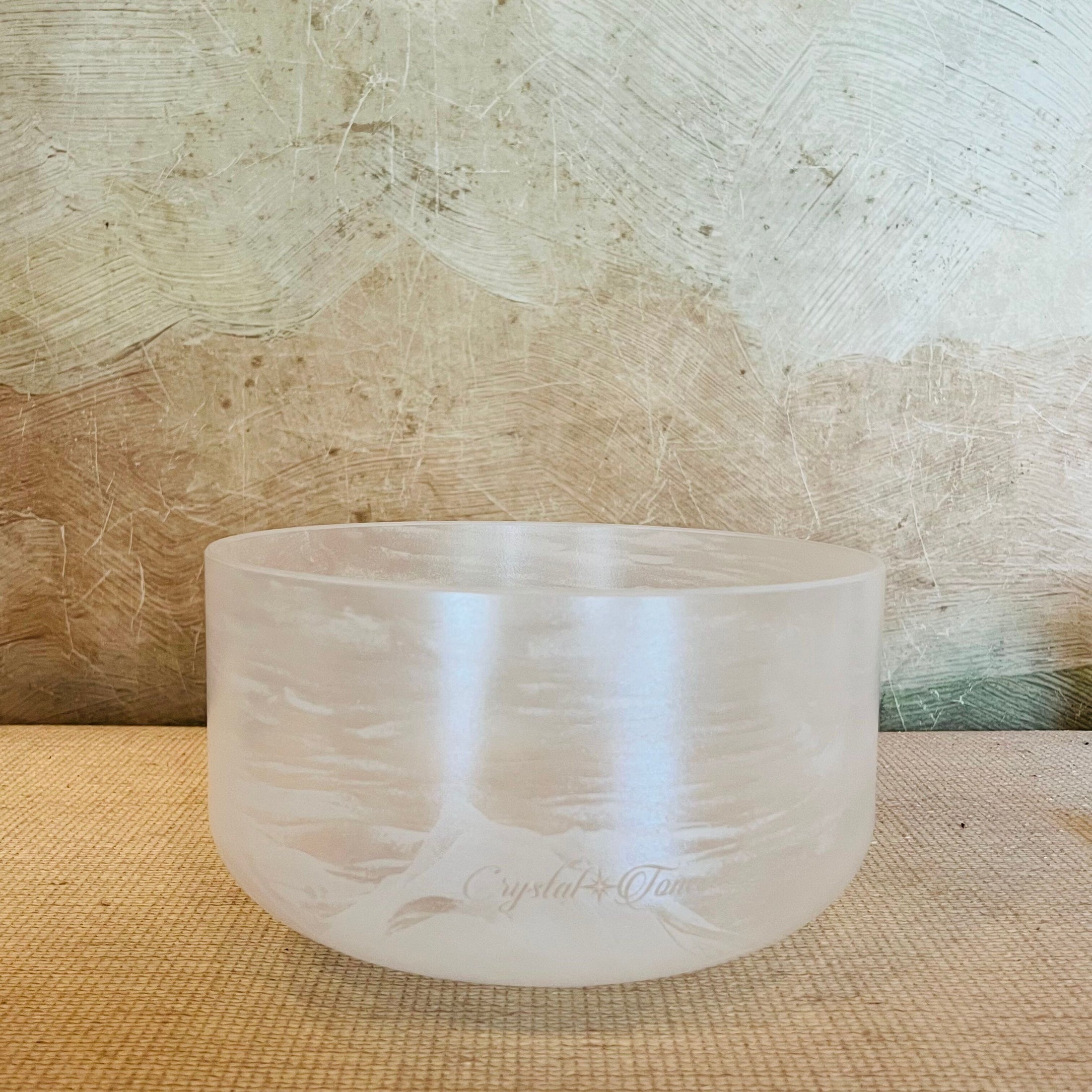 Clear crystal singing bowl on a textured surface with a neutral background