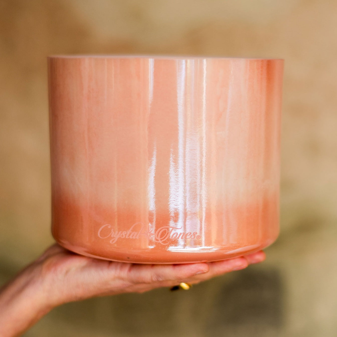 Hand holding a pink crystal singing bowl with 'Crystal Tones' branding on a blurred background