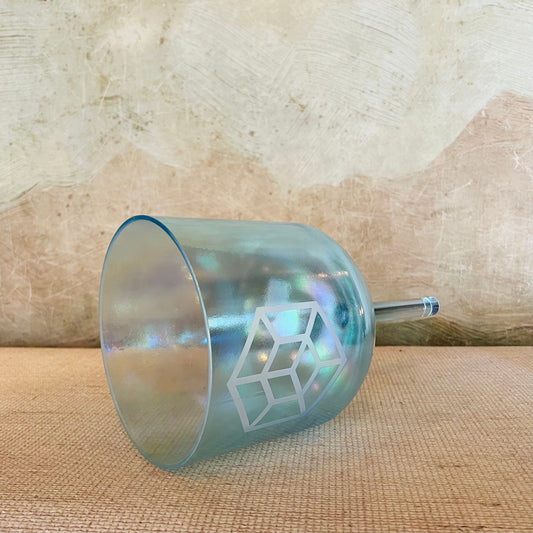 Teal crystal sound bowl with geometric design on a textured beige surface