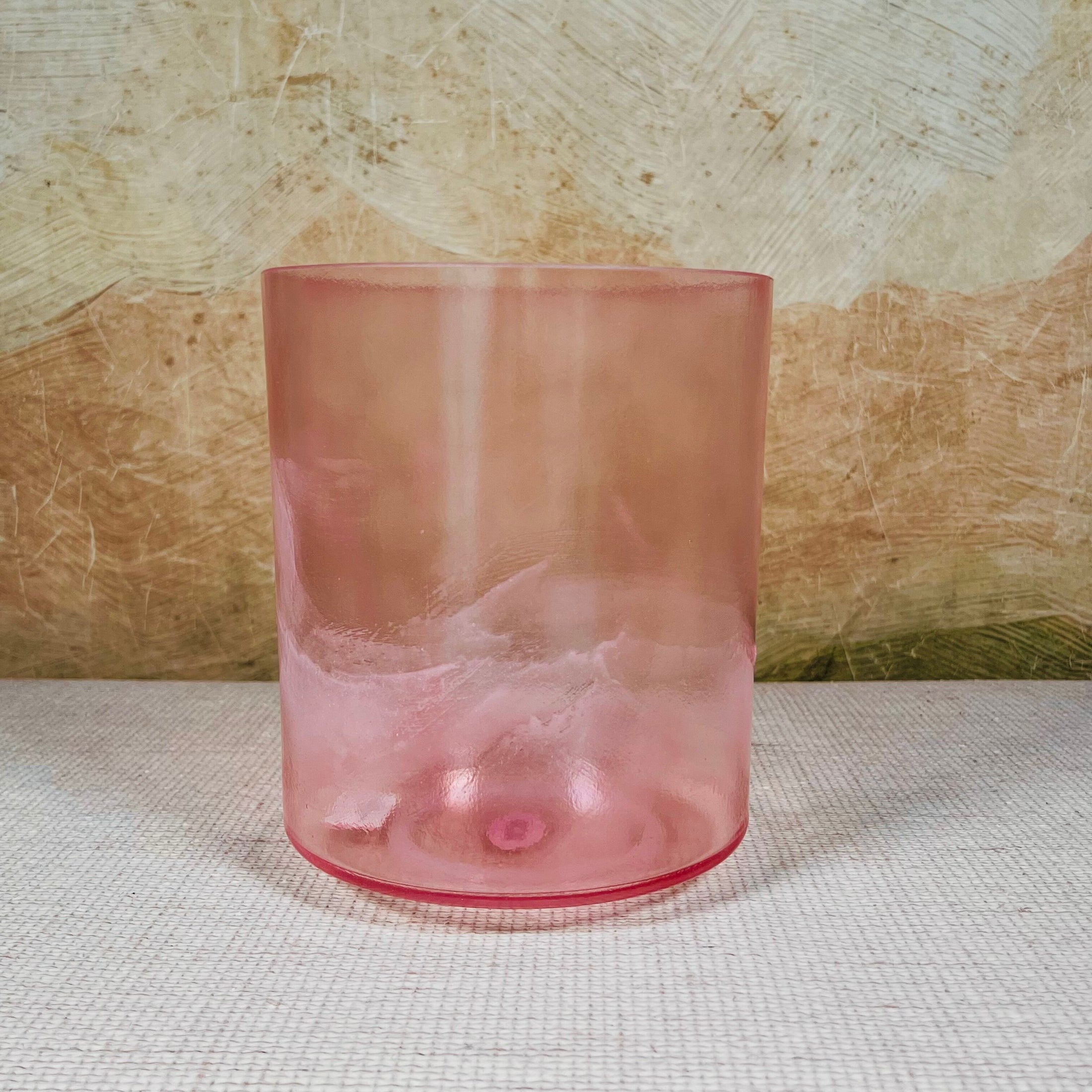 Pink crystal sound bowl on a textured surface with a neutral background