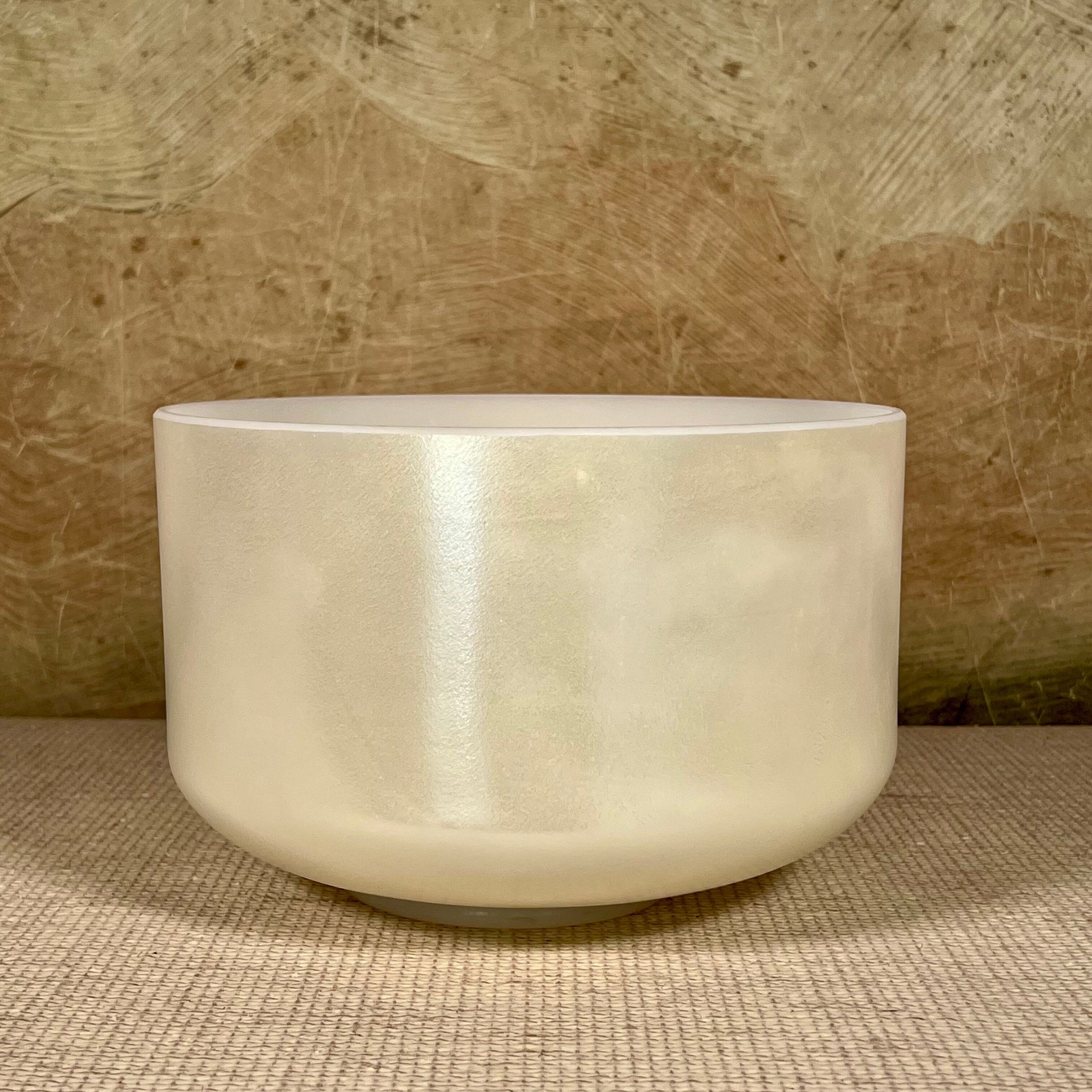 White crystal sound bowl on a textured surface with a neutral background