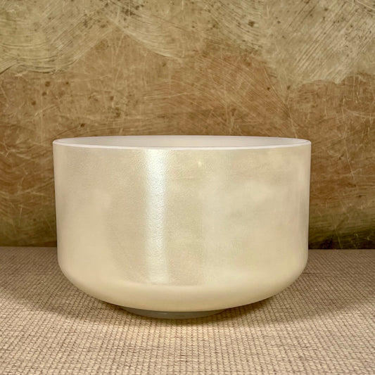 White crystal sound bowl on a textured surface with a neutral background