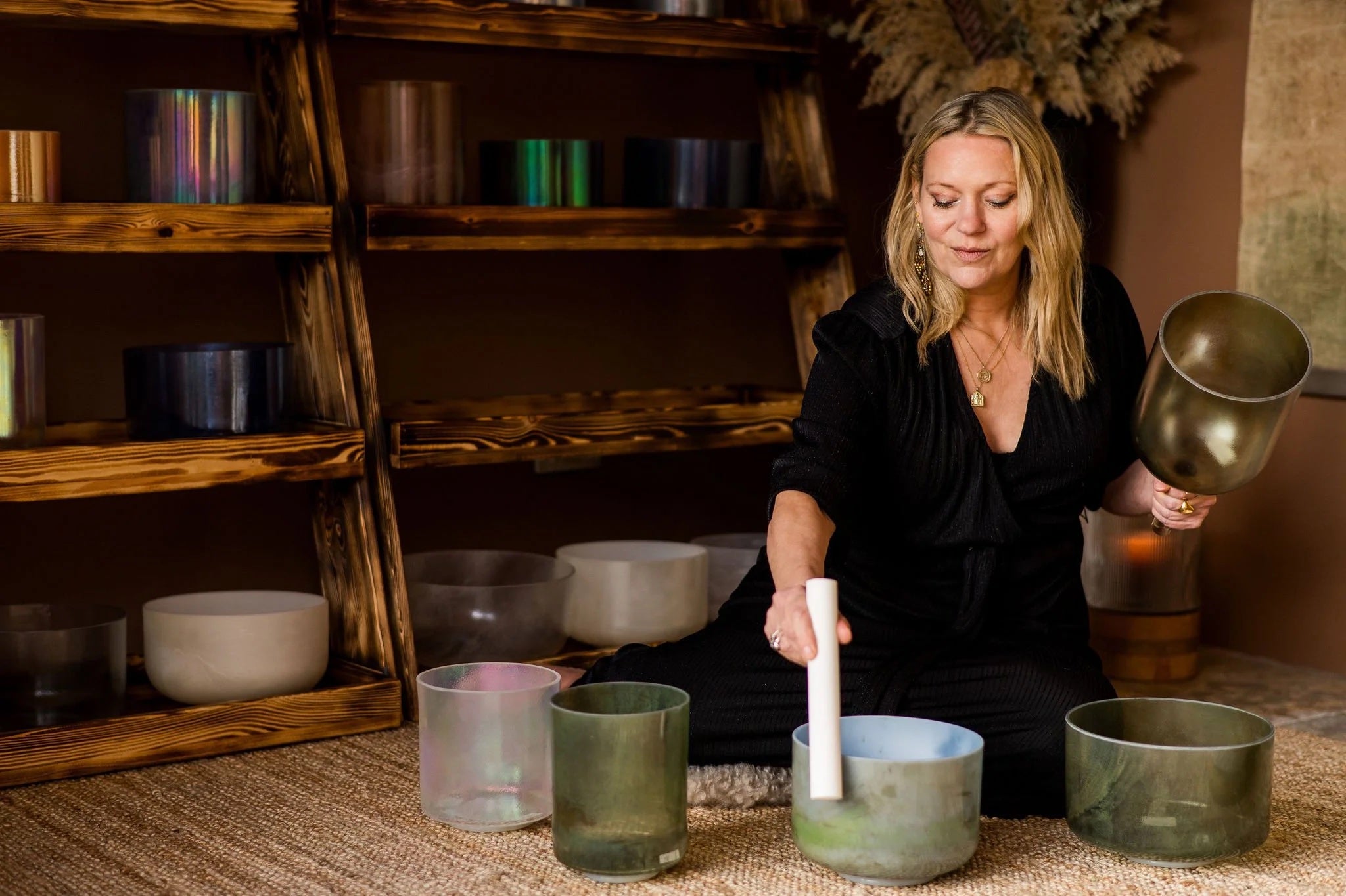 Woman - Kate - playing a set of singing bowls in a room with wooden shelves while looking down.