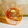 Load image into Gallery viewer, Round orange crystal sound bowl with geometric design on a textured surface
