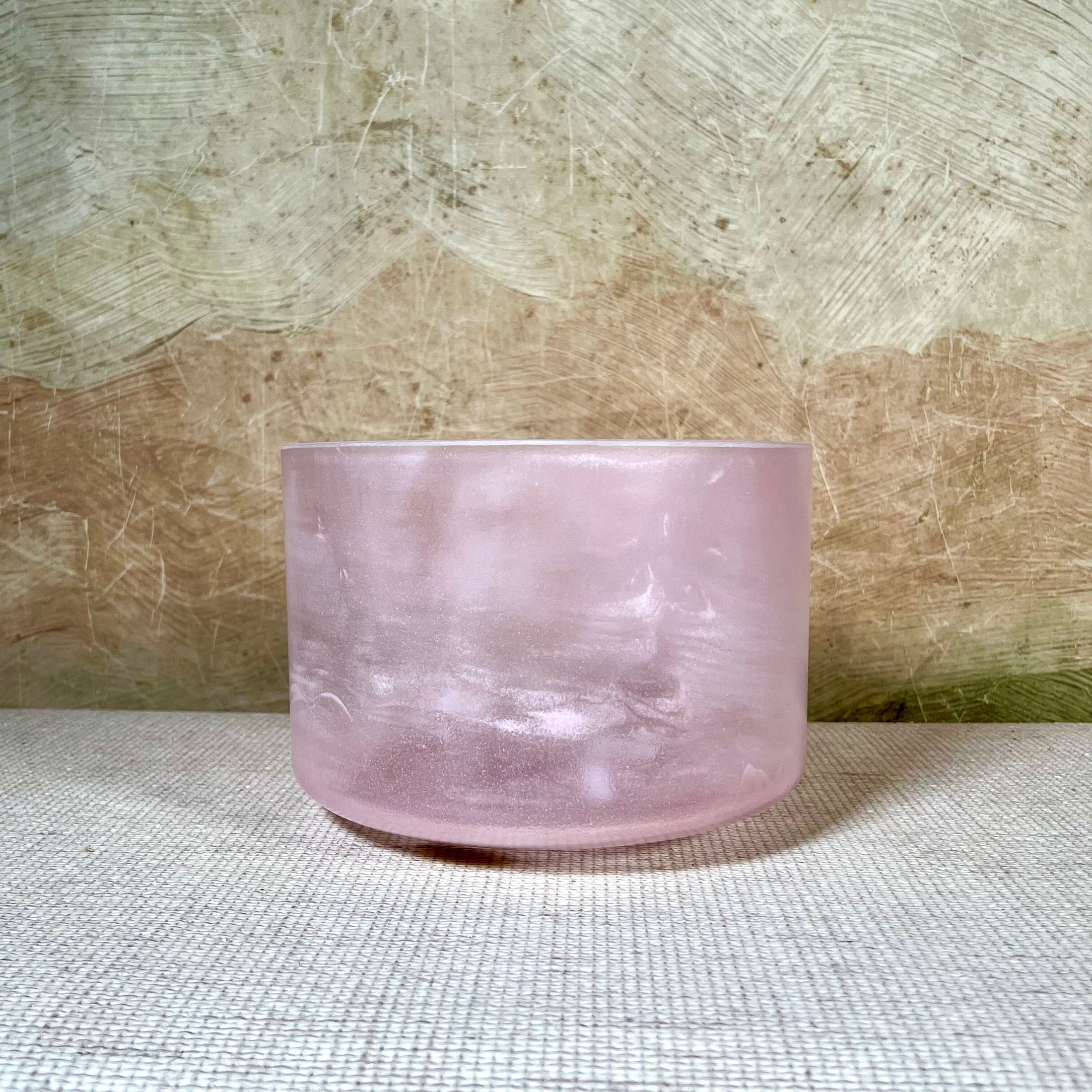 Pink crystal sound bowl on a textured surface with a neutral background