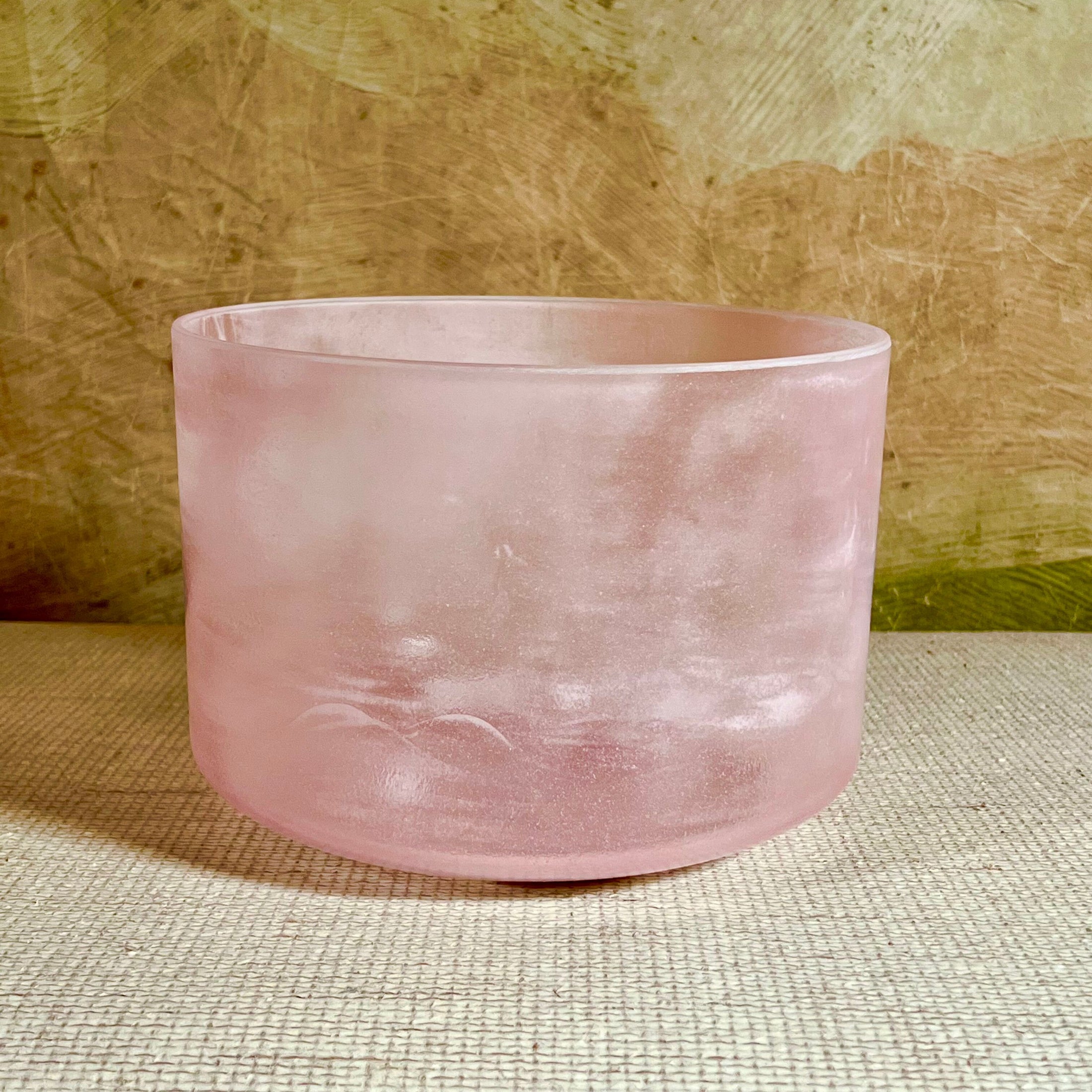 Pink crystal sound bowl on a textured surface with a wooden background