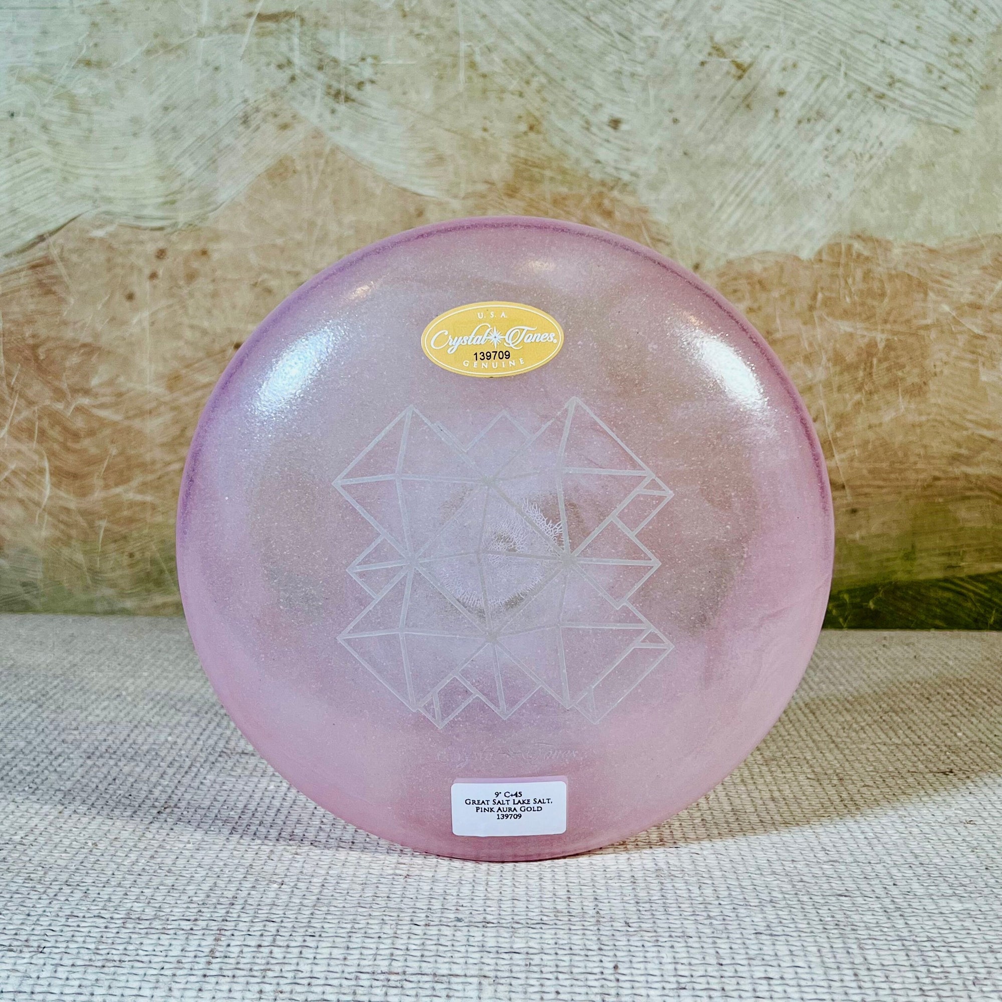 Pink crystal sound bowl with geometric design on a textured surface