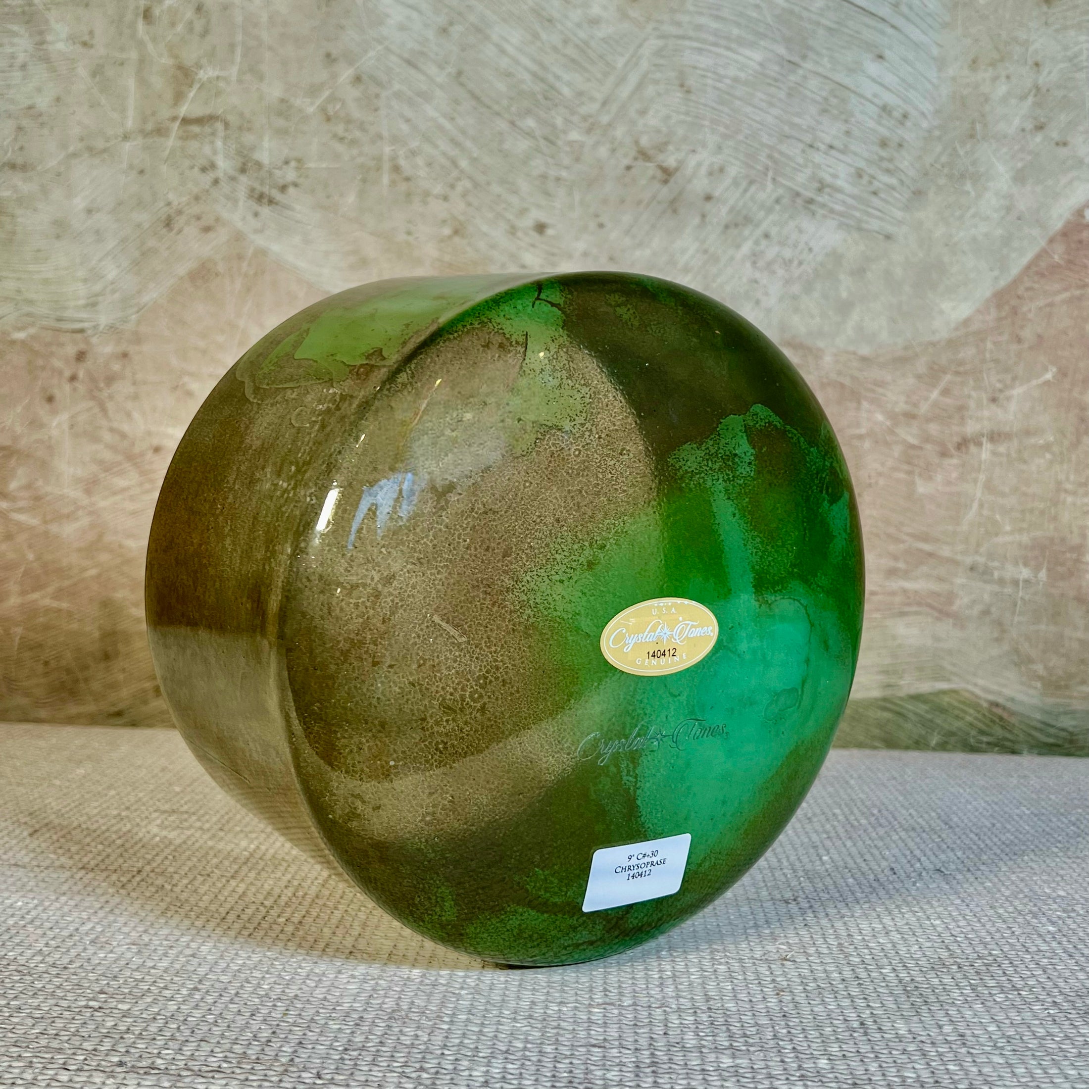 Green crystal sound bowl with a Crystal Tones label on a textured surface