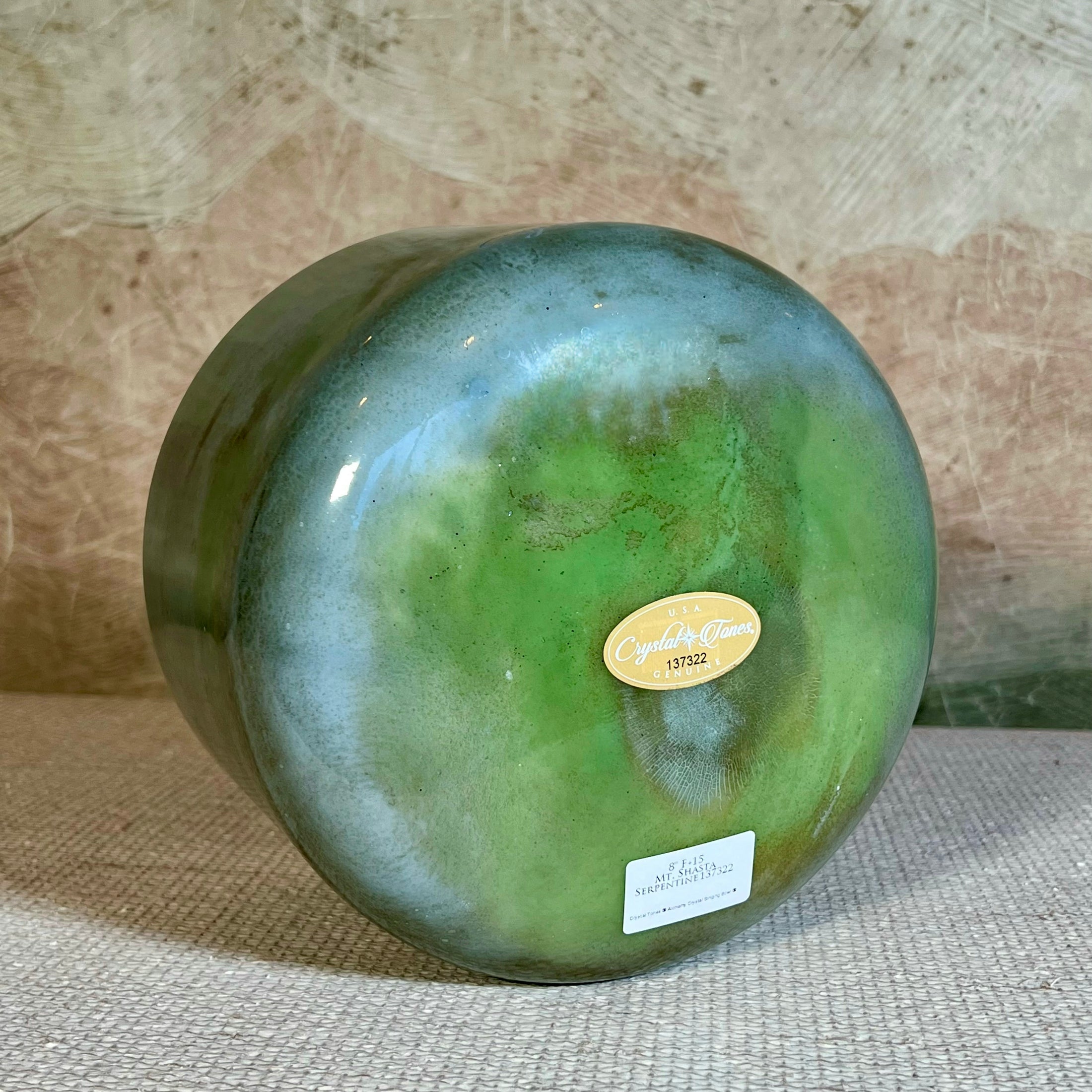 Green crystal sound bowl with a gold Crystal Tones label on a textured surface