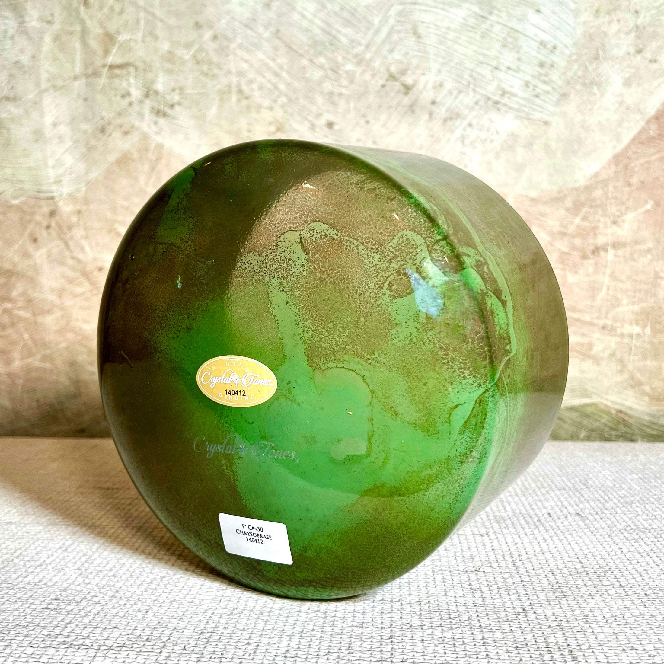Green crystal sound bowl with a label on a textured surface
