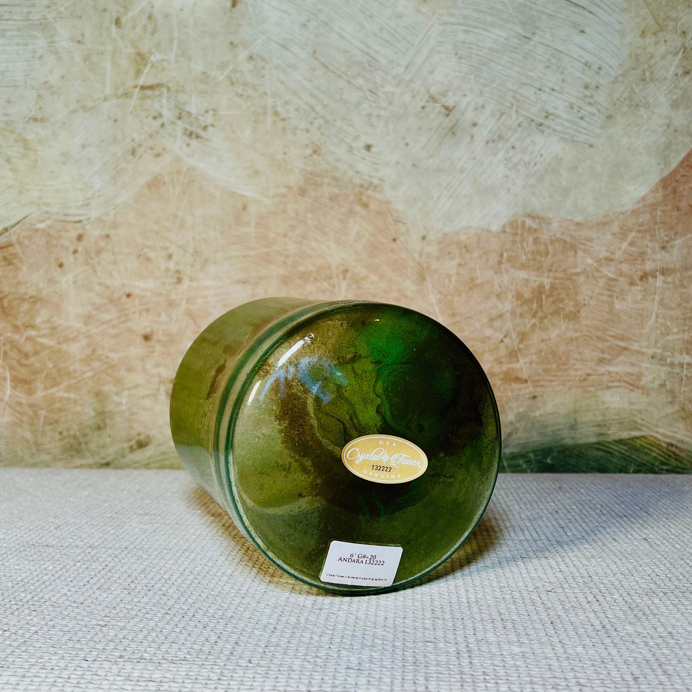 Green crystal sound bowl with a label on a textured surface