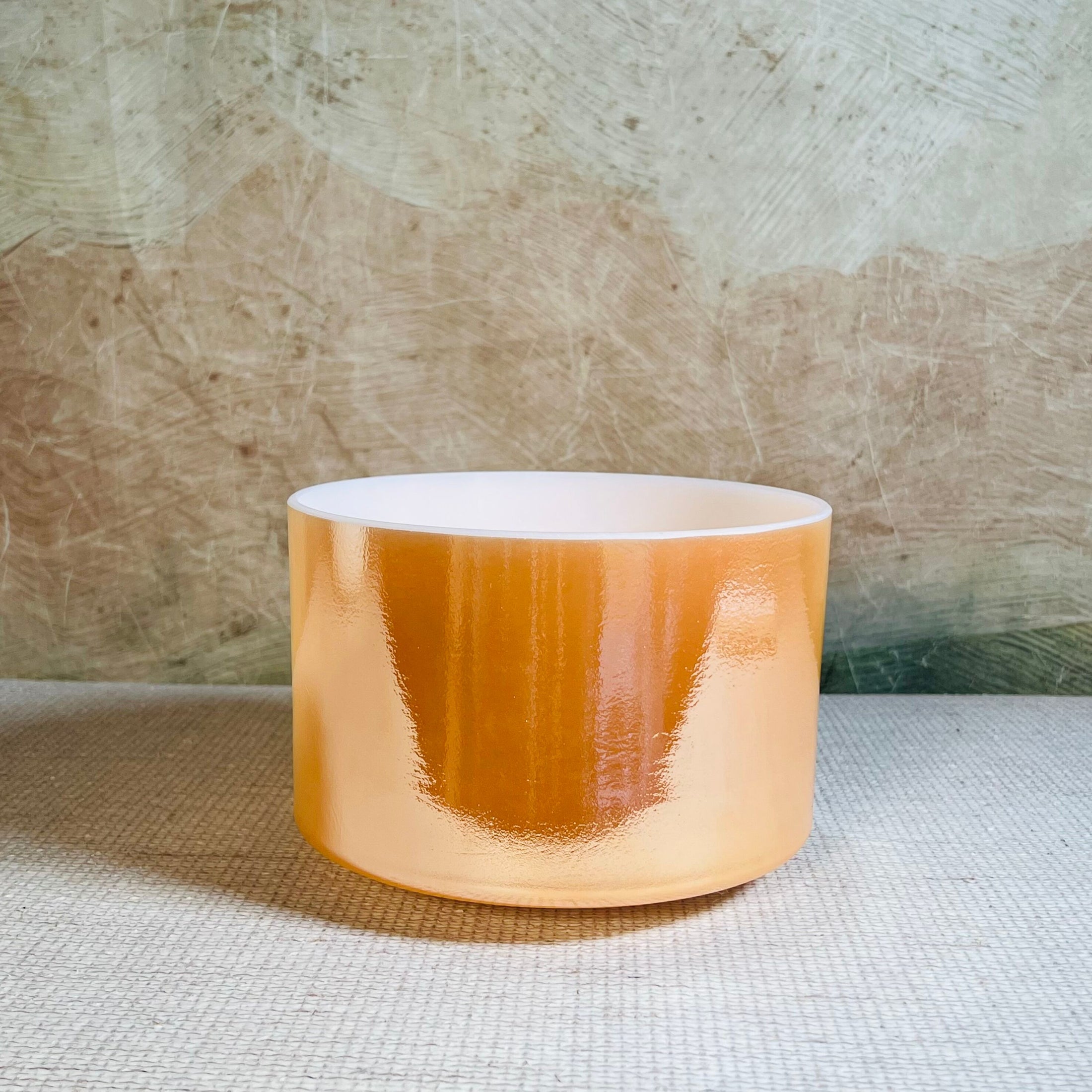 Cylindrical crystal sound bowl with orange glaze on a textured surface