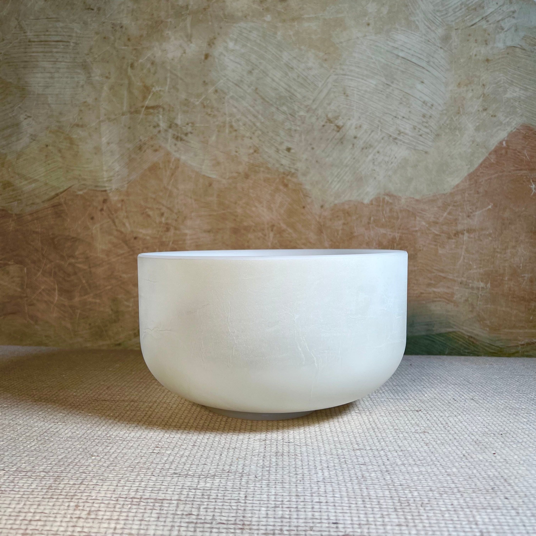 White crystal sound bowl on a textured surface with a beige background
