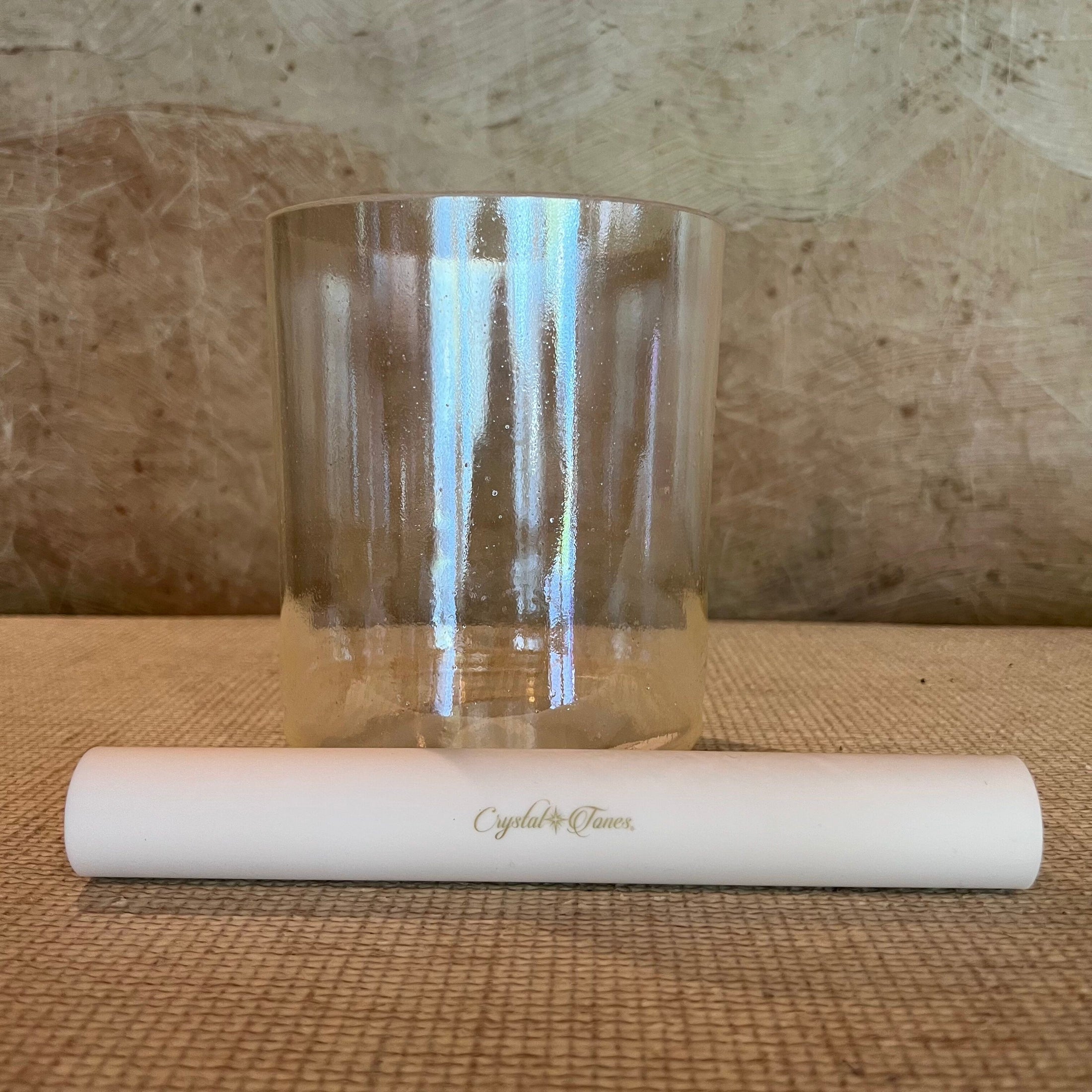 Clear crystal sound bowl with white sonic mallet on a textured surface