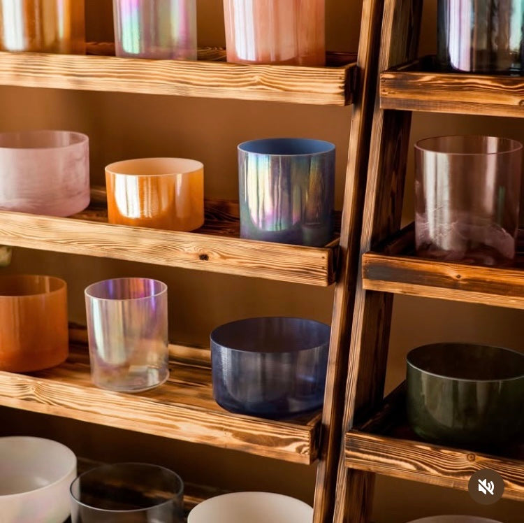 Wooden shelf with various colorful crystal singing bowls on a neutral background