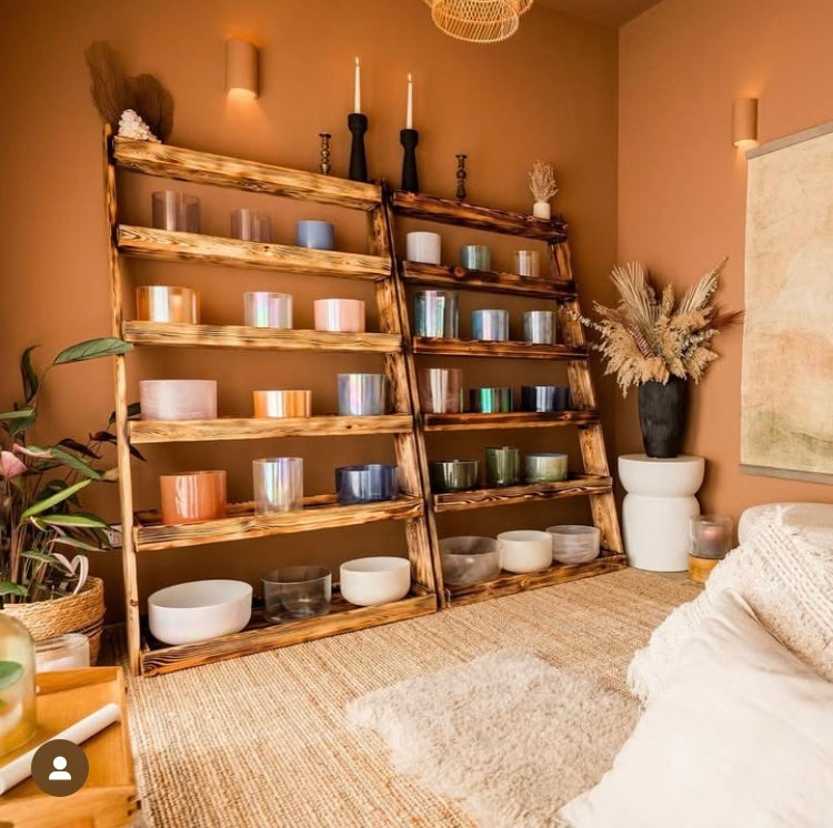 Wooden shelf with various crystal singing bowls and candles in a room with a warm colour palette.